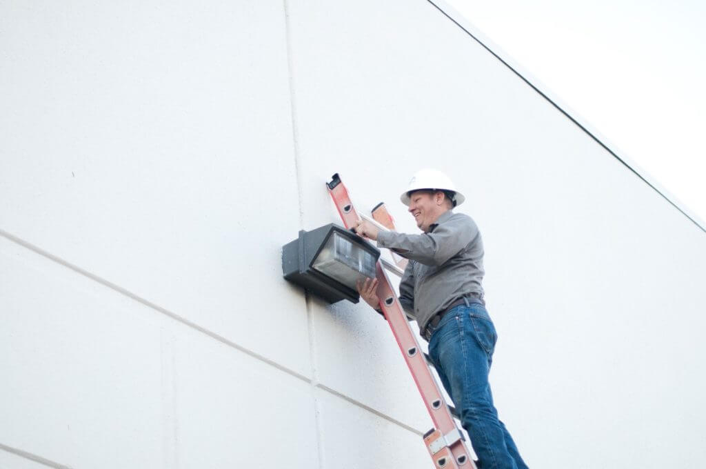 BMP Employee replacing outside building light on a ladder
